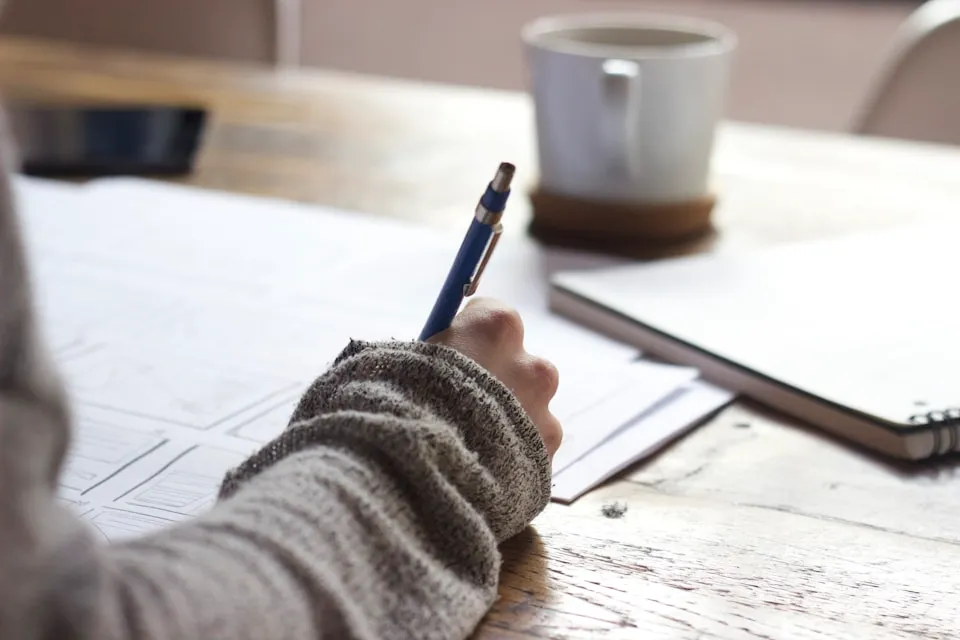 Persona joven escribiendo en una libreta con una taza de café cerca